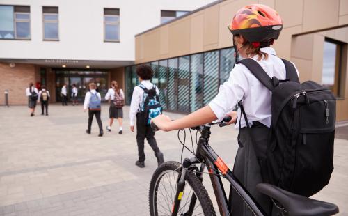 Pupil walking a bike towards a school building