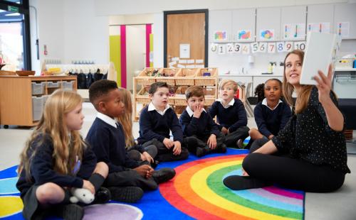 Young pupils sitting on a mat in front of a teacher