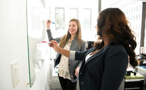 Two people writing on a whiteboard