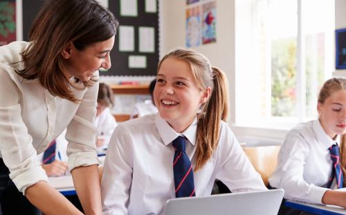 Teacher talking to secondary age pupil using a laptop