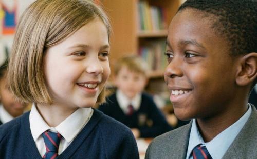 Two primary-age pupils looking at each other smiling