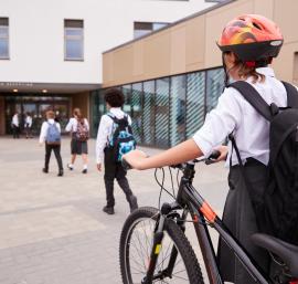 Pupil walking a bike towards a school building